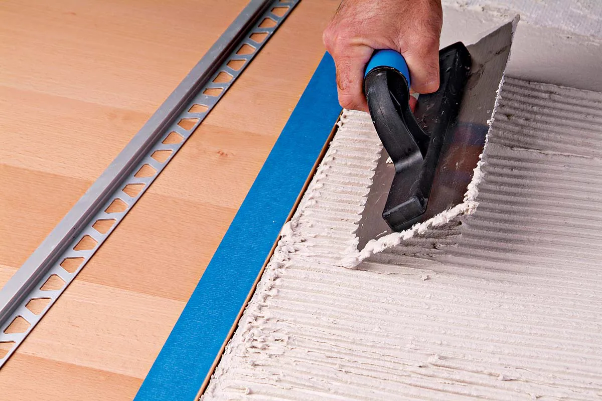 Installing tile edge trim beside a prepared adhesive bed