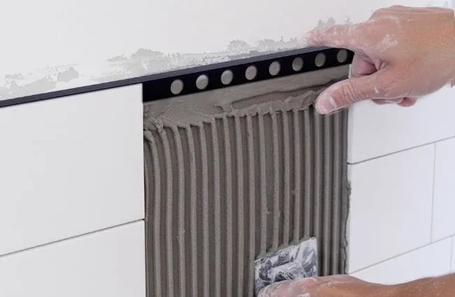 Embedding the perforated anchoring leg of metal tile edge trim into tile adhesive